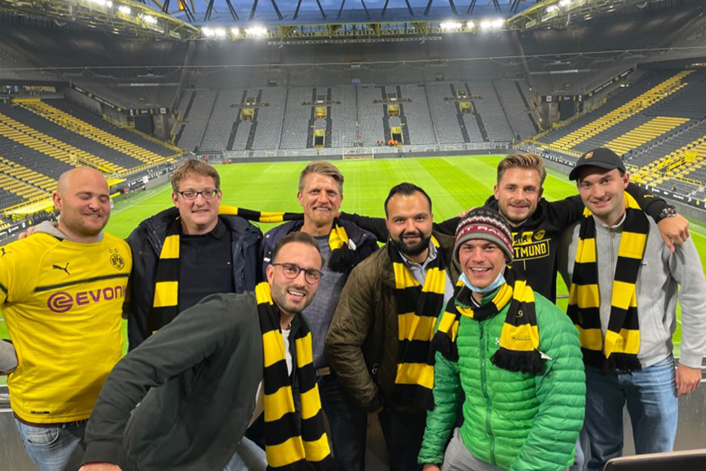 Eine Männergruppe steht im BVB-Stadion, hat Dortmundschale um und lacht in die Kamera