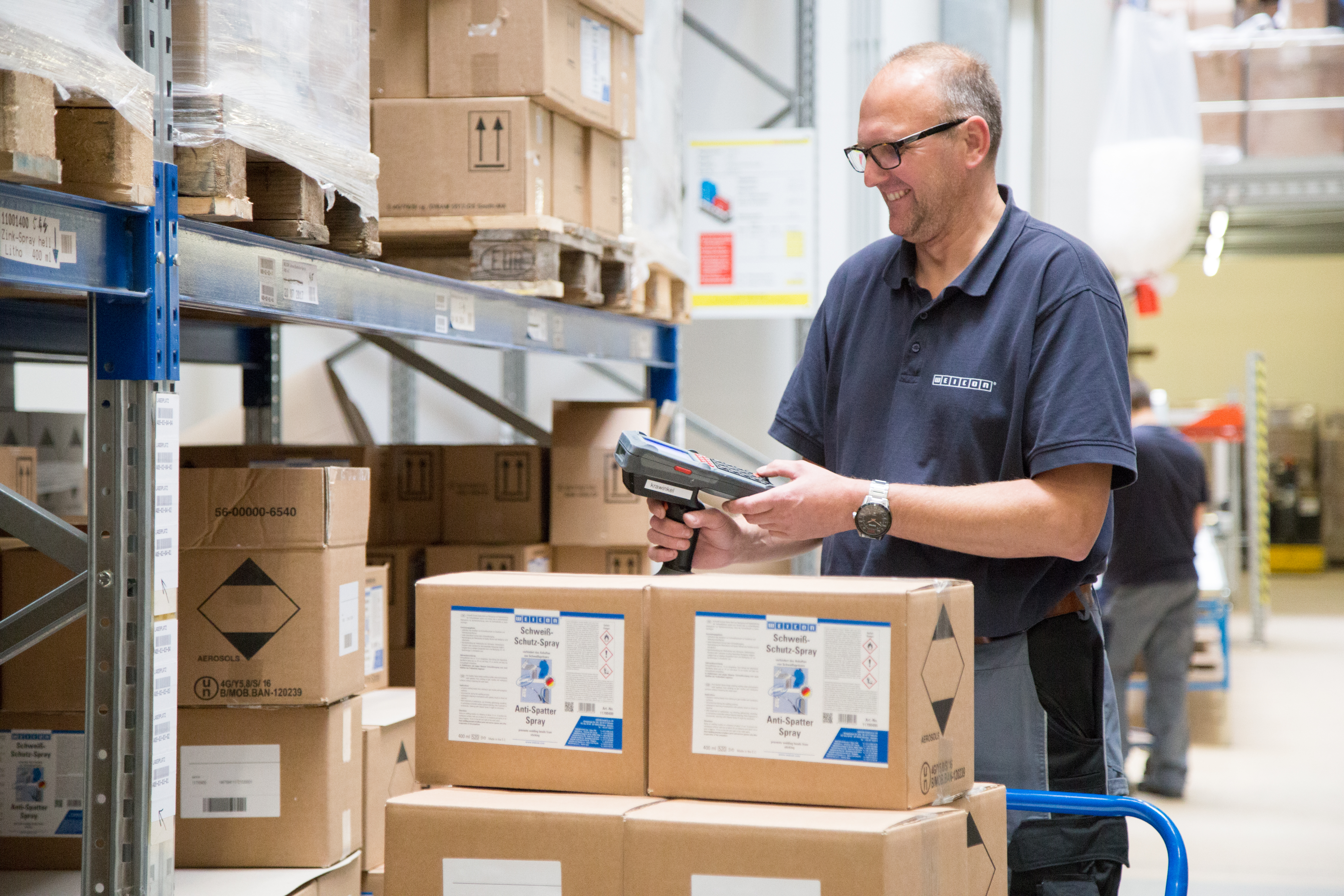 Ein Mann arbeitet im Lager, vor ihm steht ein Wagen mit mehreren Kartons drauf