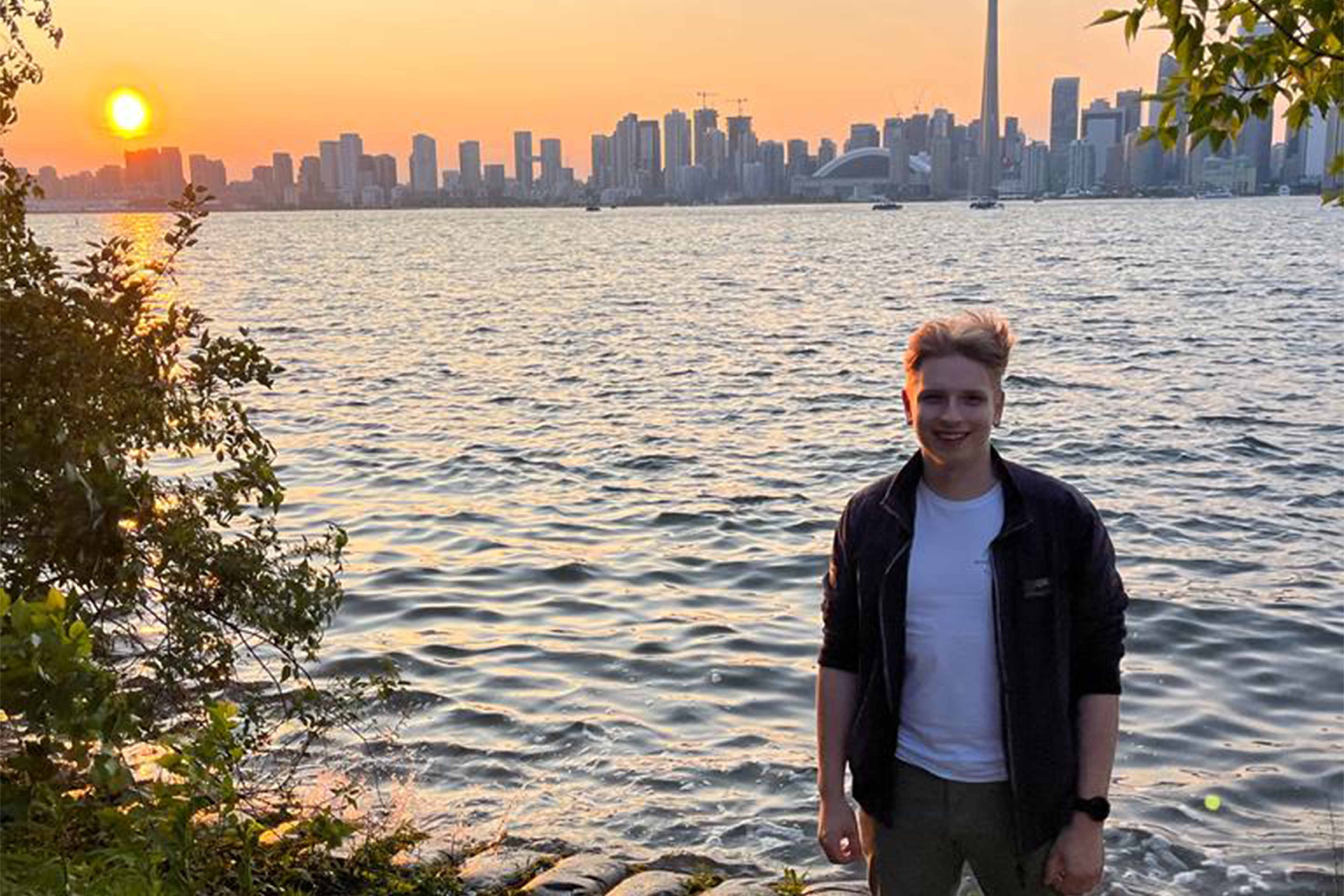Ein Mann steht bei Sonnenuntergang vor dem Wasser und im Hintergrund ist eine Skyline