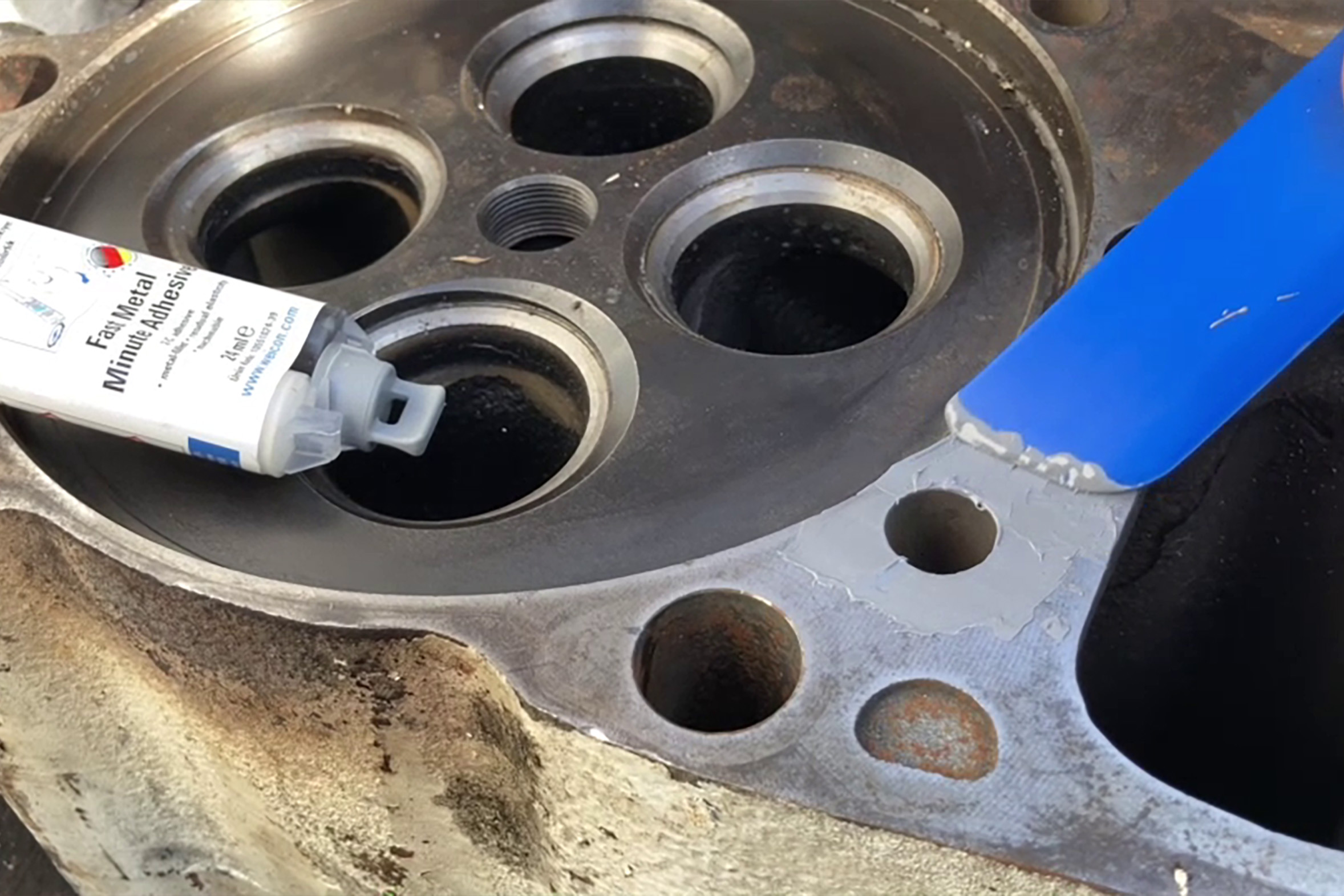 Ein Motorblock mit zylindrischen Löchern. Darauf liegt der Weicon Fast-Metal-Minutenkleber.