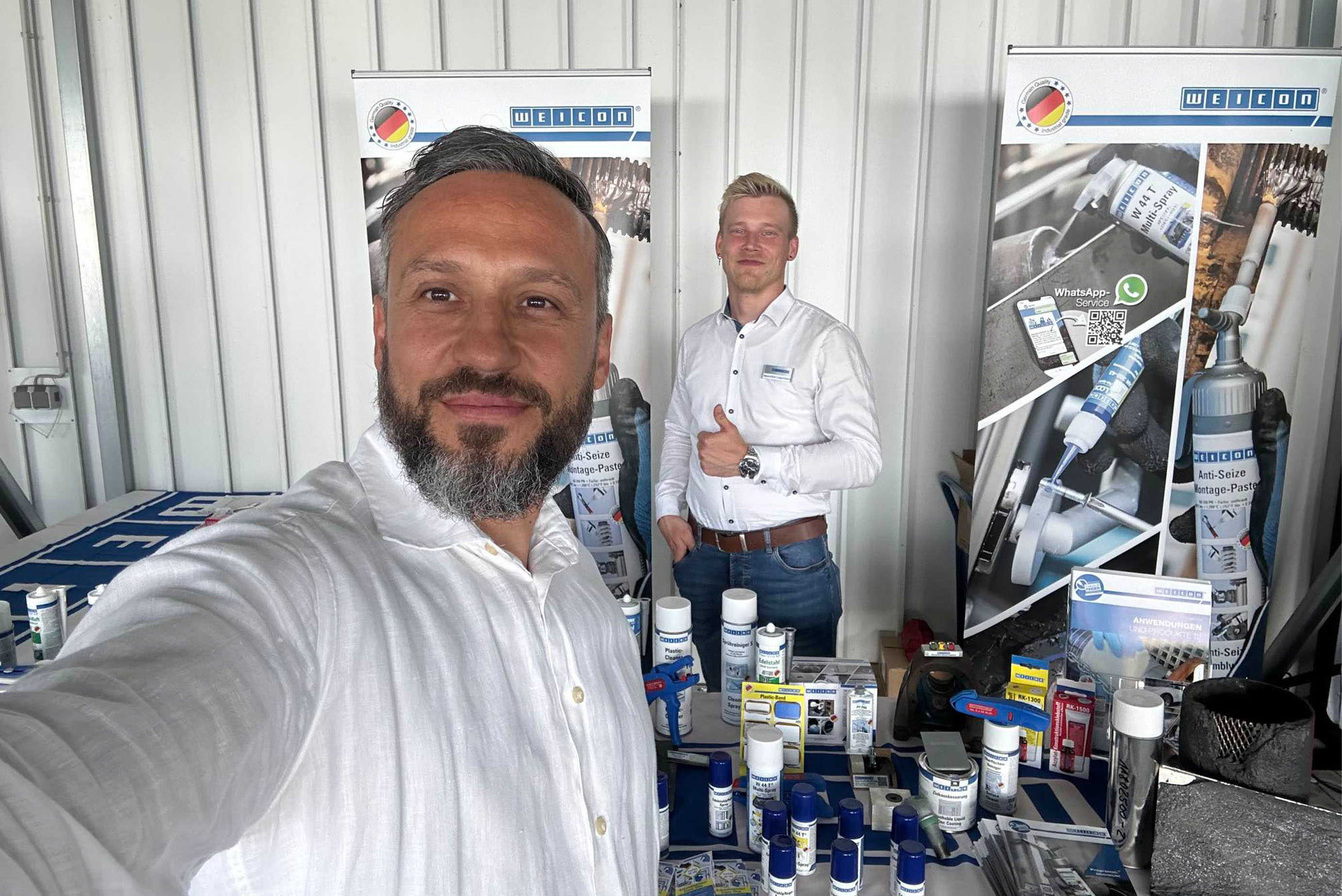 Zwei Männer machen ein Selfie, auf denen ein Stand mit Weicon Produkten zu sehen ist