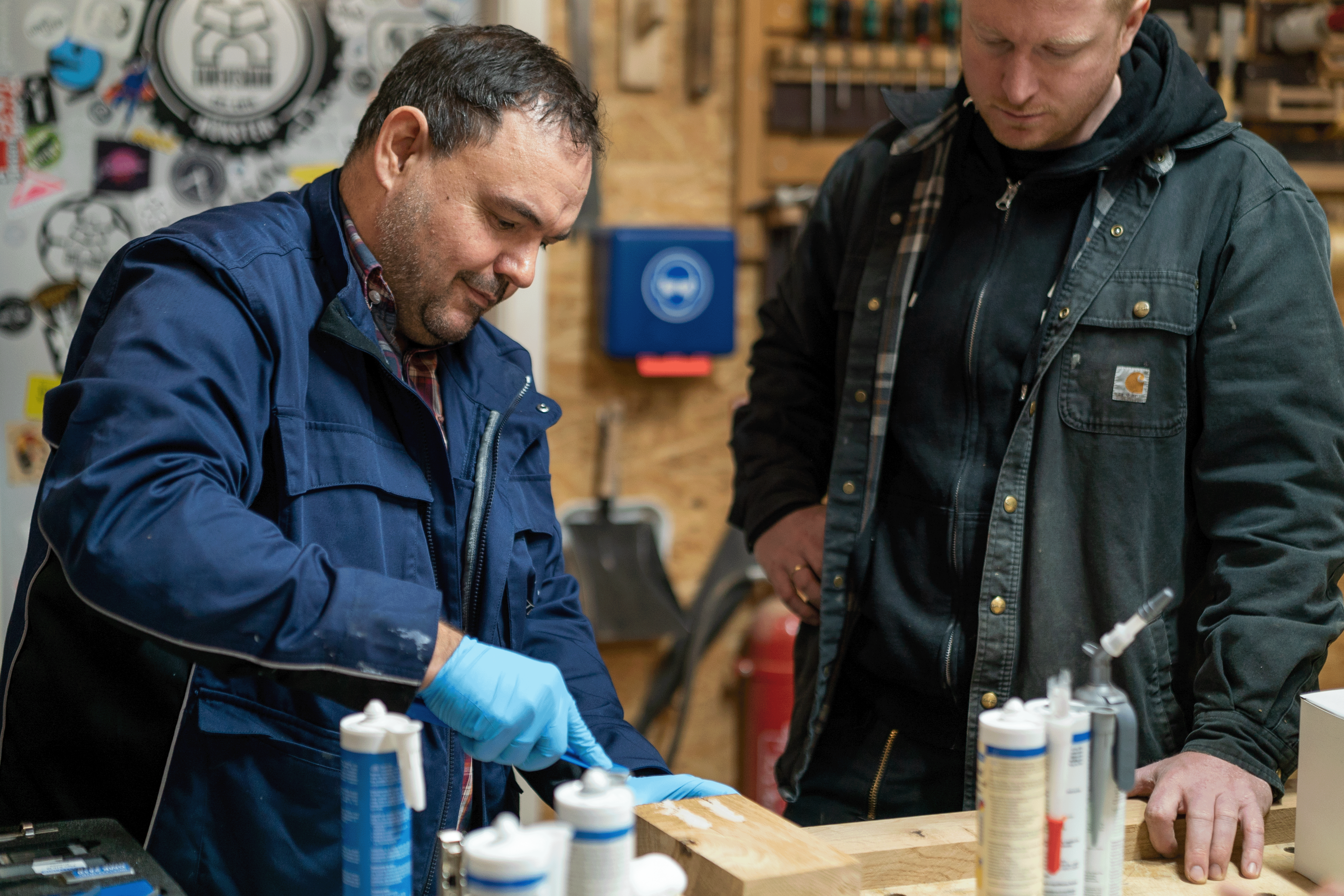 Zwei Männer stehen in einer Werkstatt, der eine hat einen Spatel in der Hand, der andere schaut zu