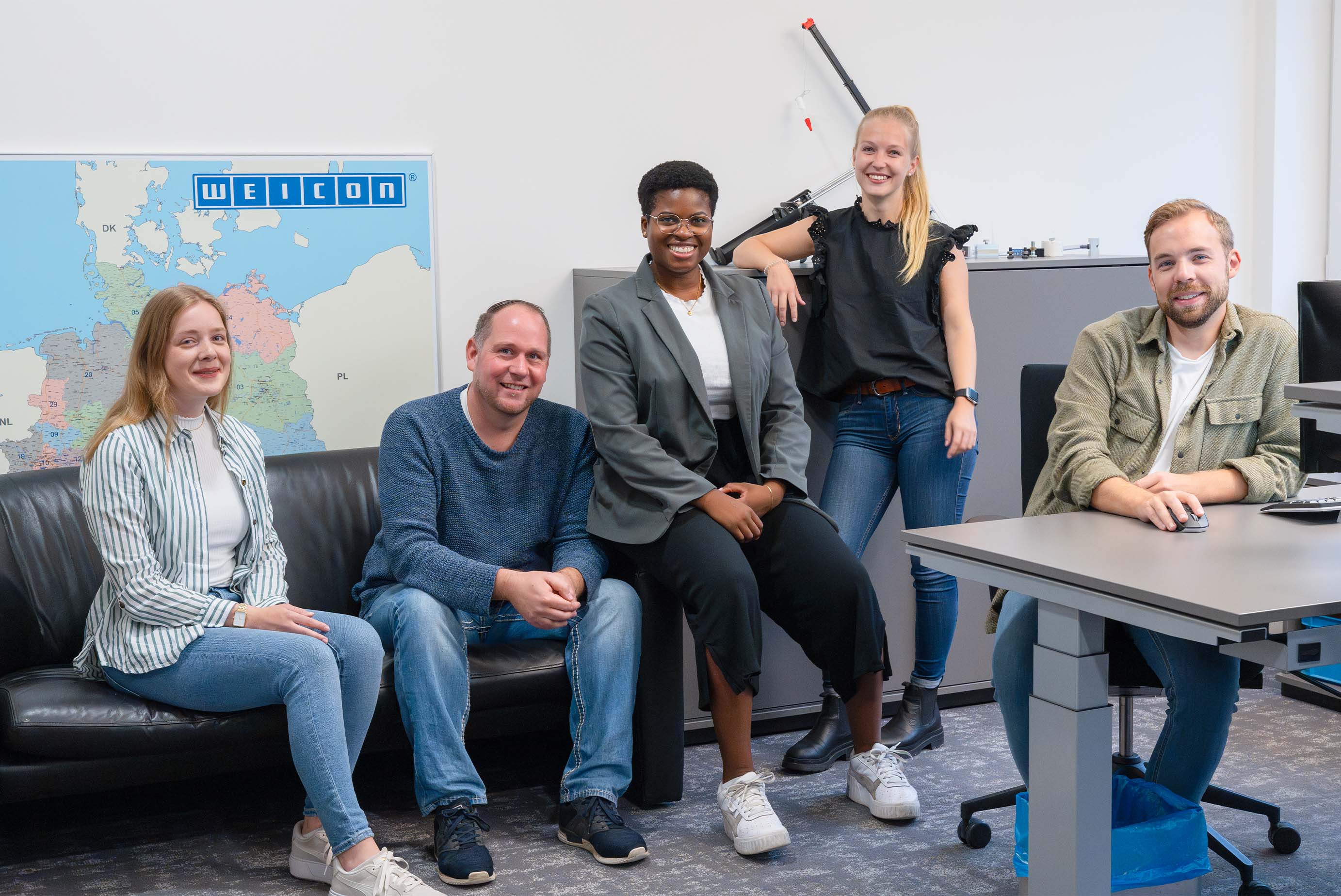 Fünf Personen sitzen in einem Büro und lachen in die Kamera